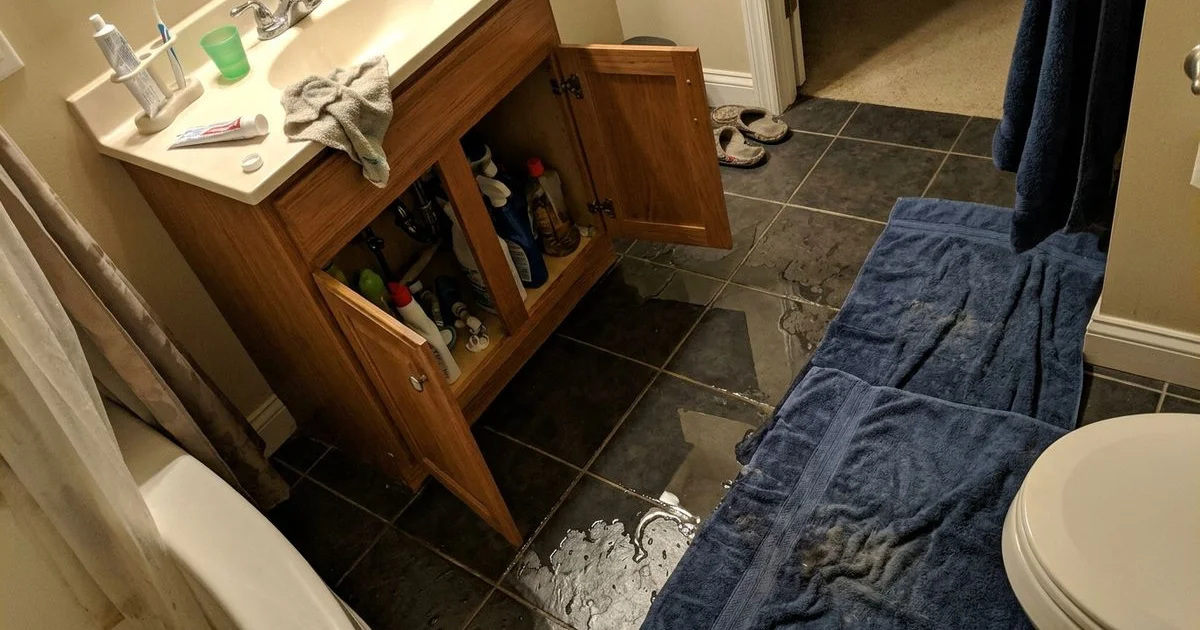 Water pooling across a tile floor near a bathroom vanity at night