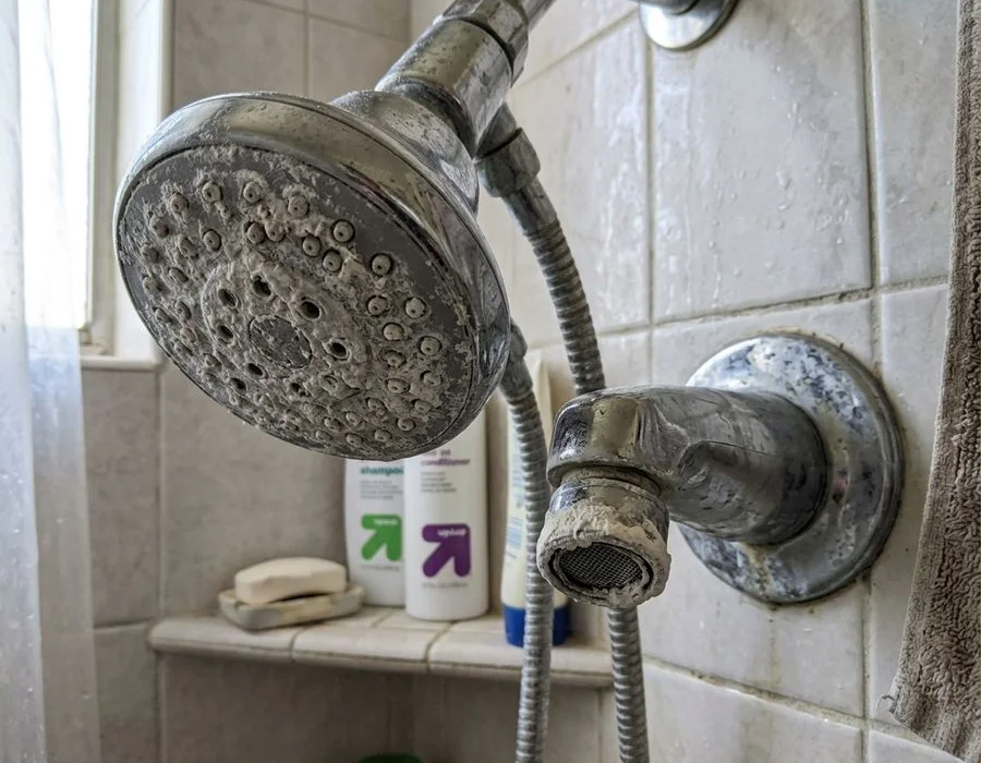 Heavy white mineral scale crusted on a shower head and faucet aerator in an Imperial Valley bathroom